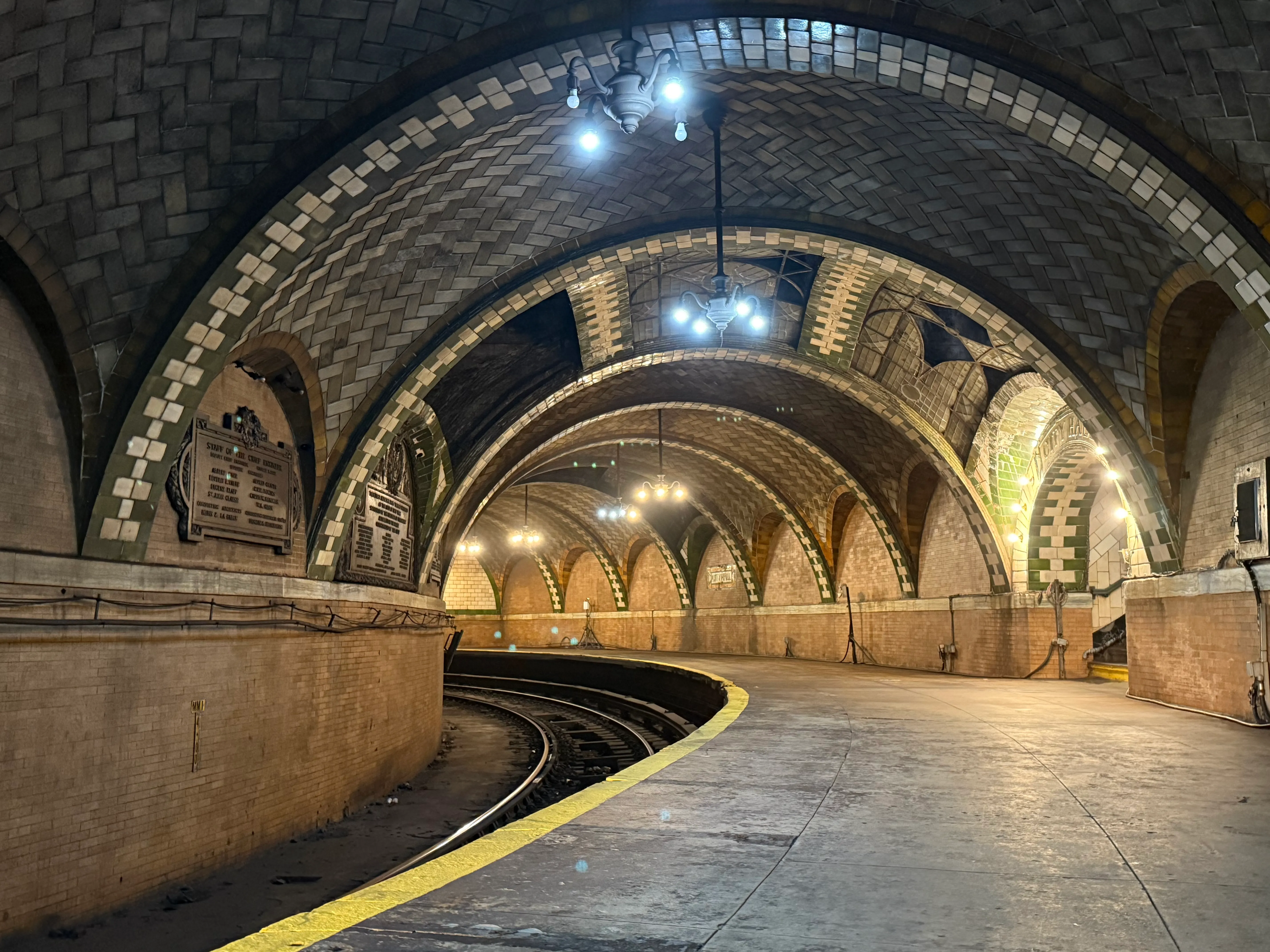 Long view down the curvy city hall station platform. Arches go overhead with green-and-white tile patterns.